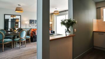 A modern kitchen with a wooden countertop, a vase with flowers, and a dining area with teal chairs and a round table.