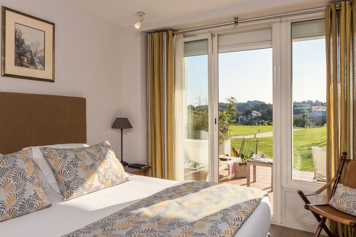 Una habitación de hotel con una cama grande, vistas al exterior, un cuadro enmarcado en la pared y una lámpara.