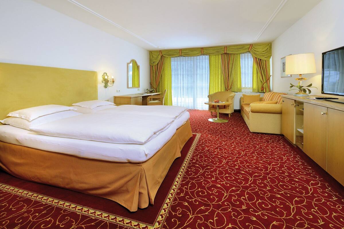 Une chambre d’hôtel avec un grand lit, un bureau, une chaise, une télévision et une fenêtre avec des rideaux.