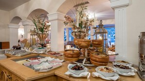 Montaje de bufé con diversos alimentos, como frutas, carnes y pasteles, dispuesto sobre una encimera de madera con jarrones decorativos y velas.