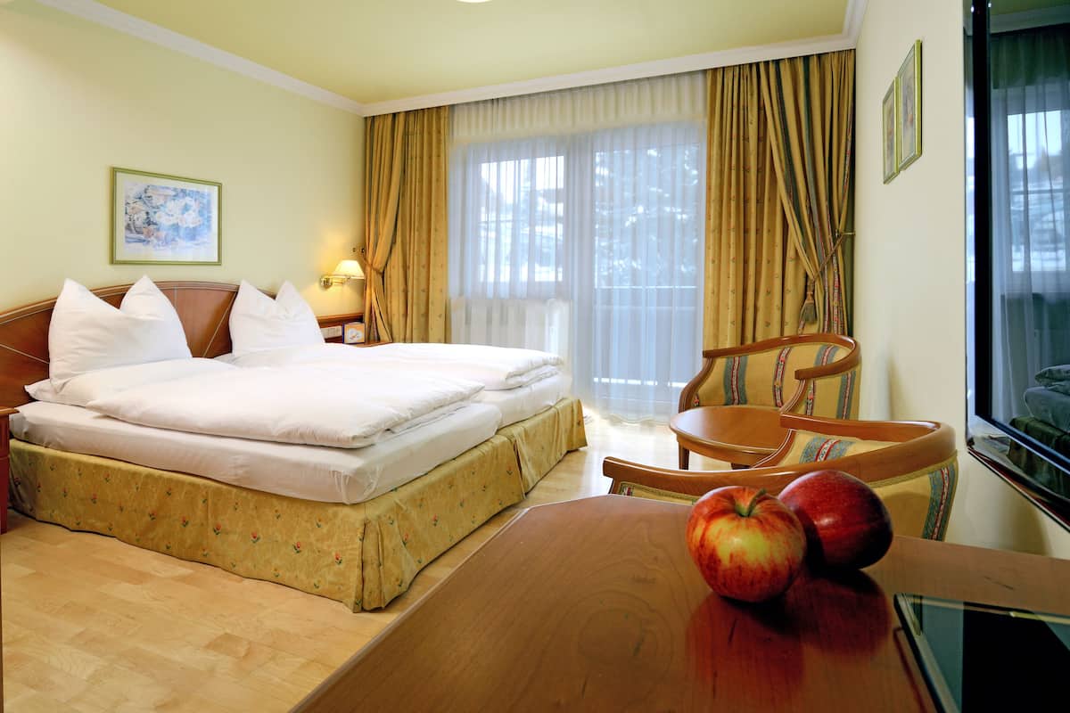 Une chambre d’hôtel avec un lit, un bureau en bois, une chaise et une fenêtre avec des rideaux.