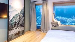 Un hotel moderno con una cama grande, vistas a una montaña nevada a través de una ventana y un cuadro de paisaje montañoso en la pared.