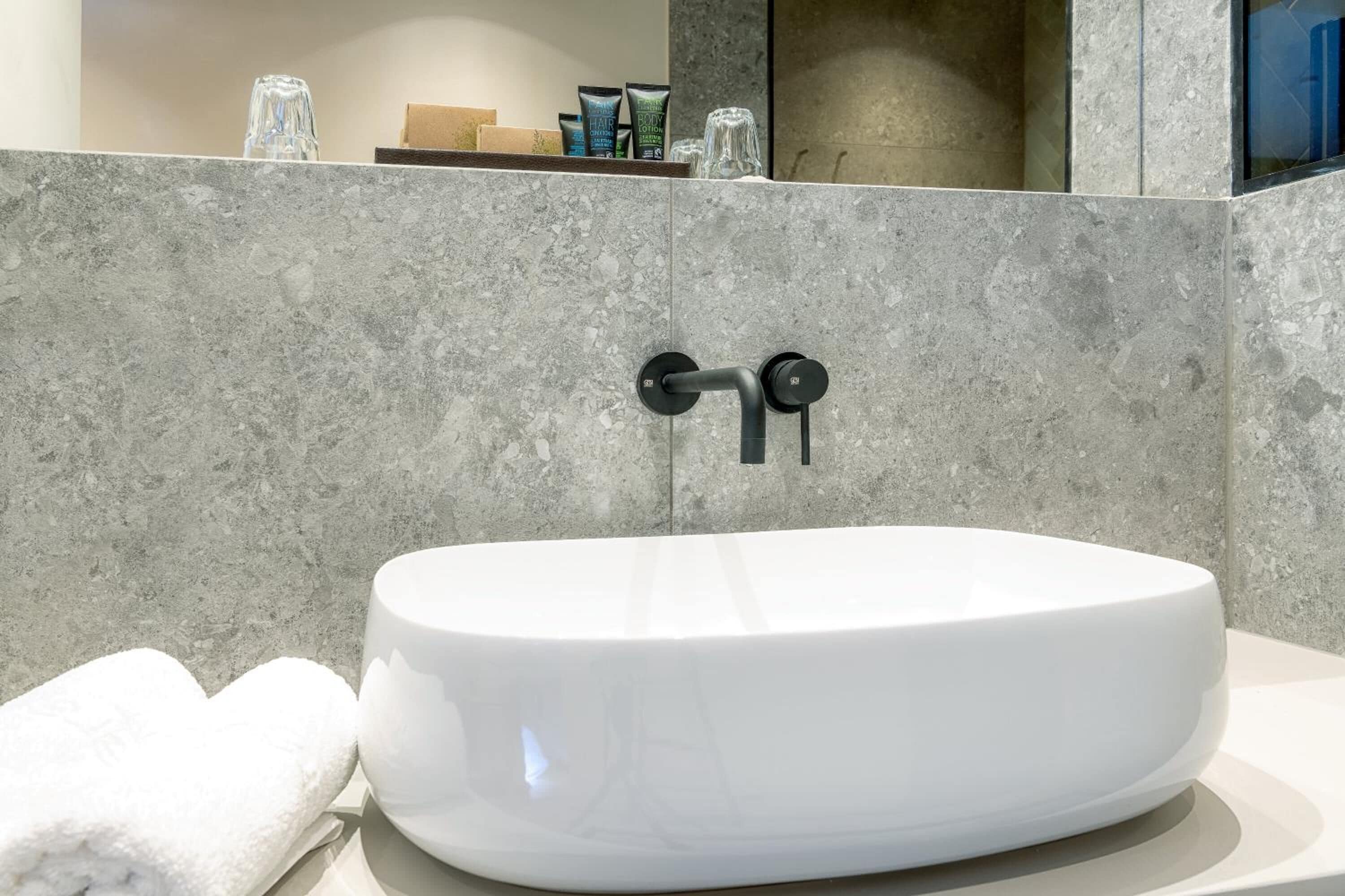 Un baño moderno con un lavamanos tipo lavabo blanco, una toalla y artículos de aseo en un estante.
