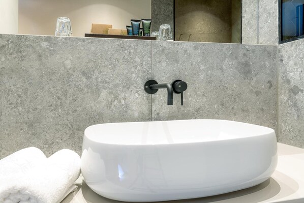 A modern bathroom with a white vessel sink, a towel, and toiletries on a shelf.