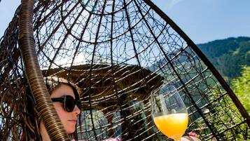 A person relaxing in a wicker chair with a glass of orange juice, overlooking a mountainous landscape.
