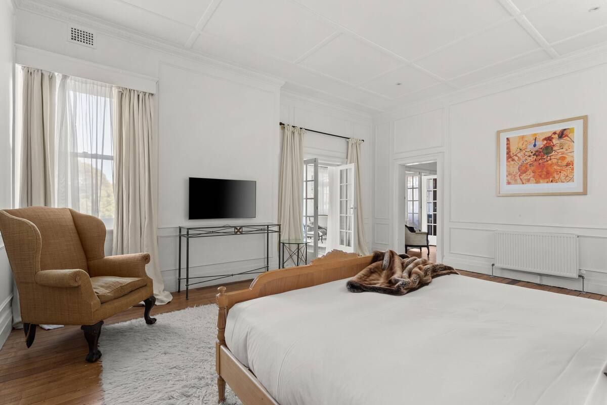 Quarto com cama grande, uma cadeira, televisão e um quadro na parede.