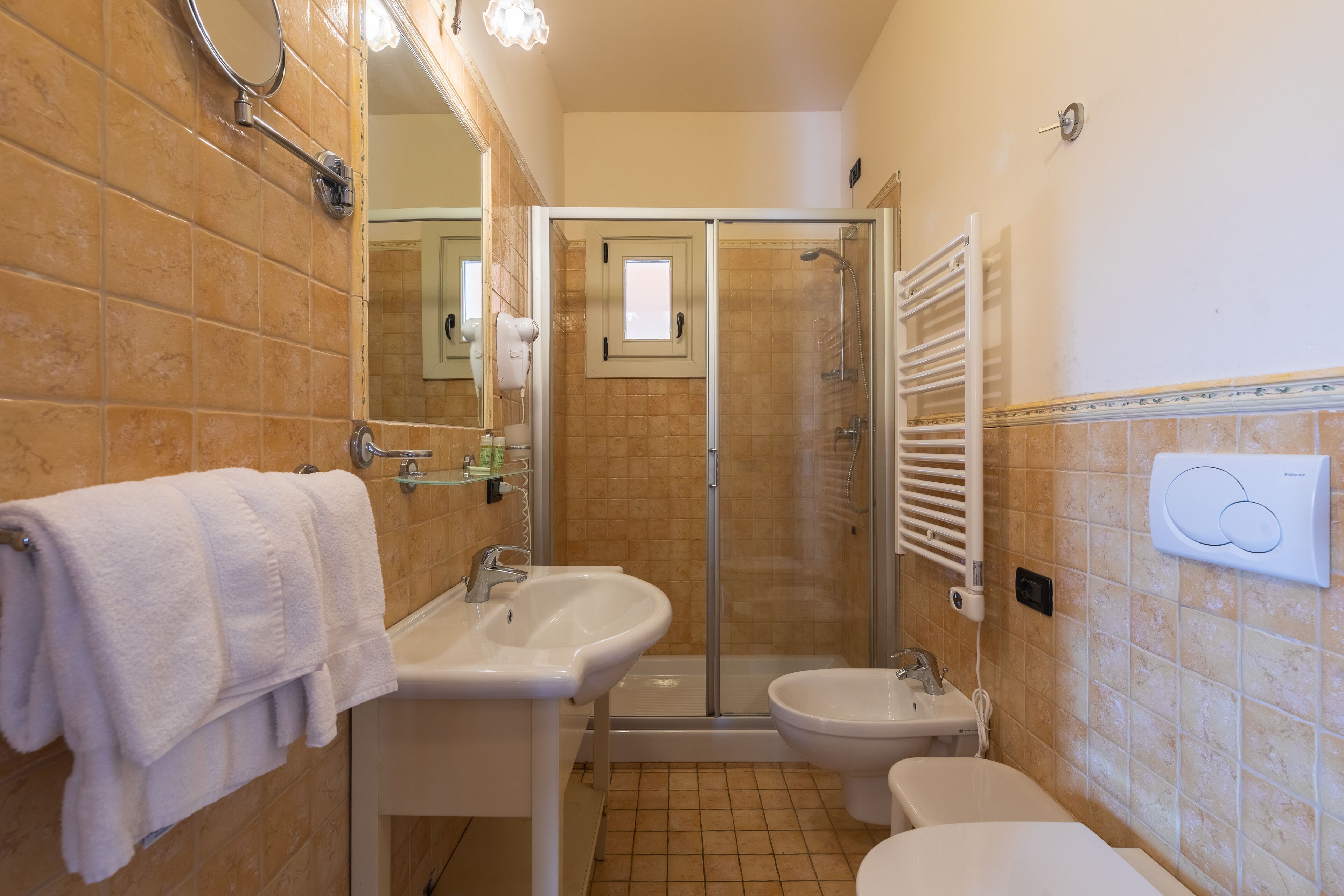 A bathroom with a glass-enclosed shower, a sink, a bidet, and a towel rack.