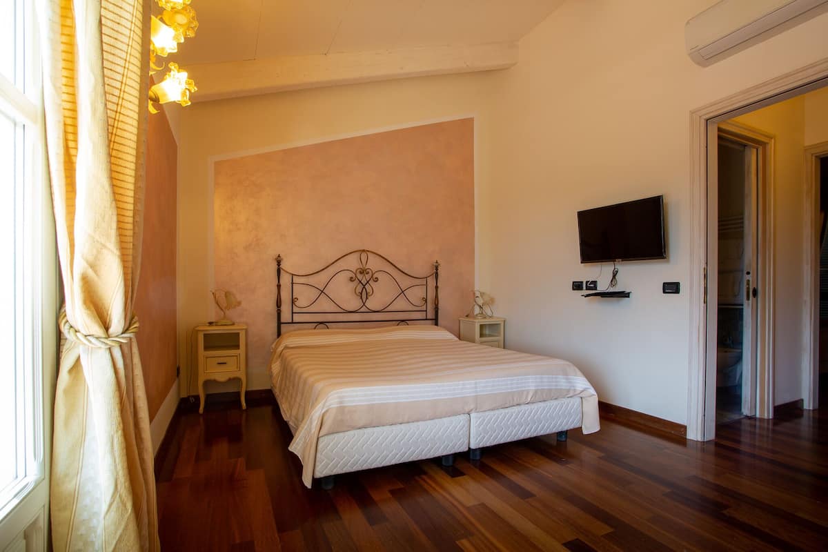 A bedroom with a bed, bedside tables, a television, and a door leading to another room.