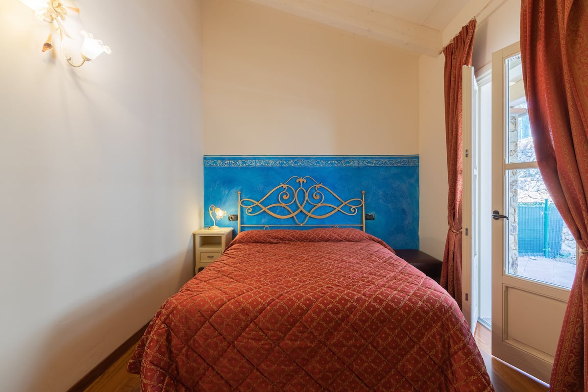 A bedroom with a bed, a nightstand, a wall-mounted light, and a window with curtains.