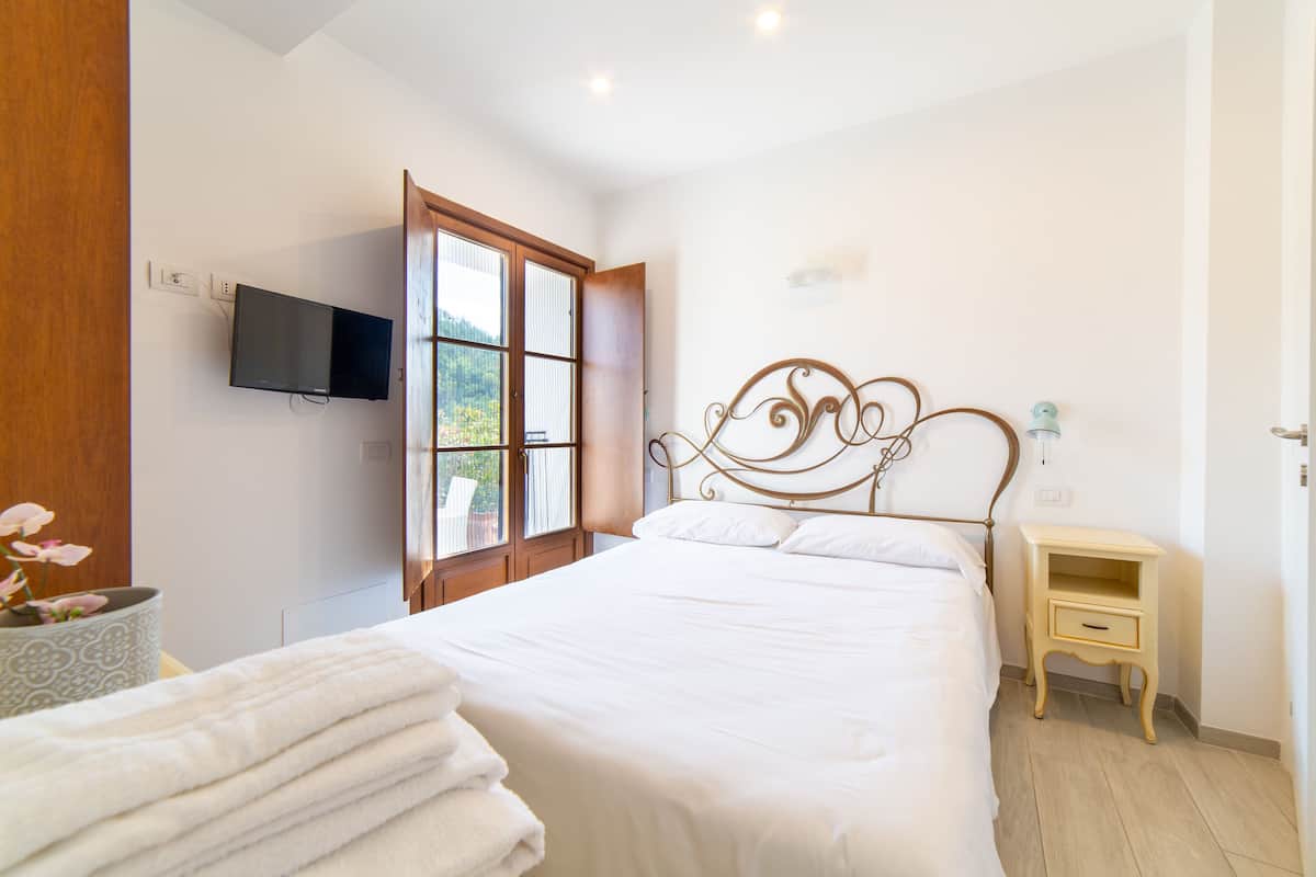 A bedroom with a bed, a TV mounted on the wall, a window with a view, and a bedside table.