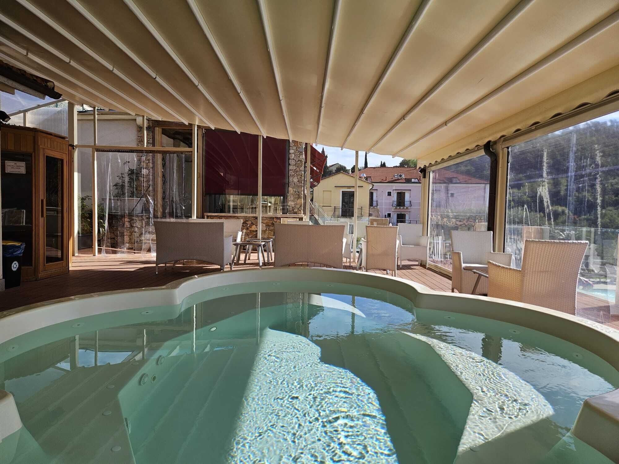 Un'area piscina con bordo curvo, mobili in vimini e un portico coperto.