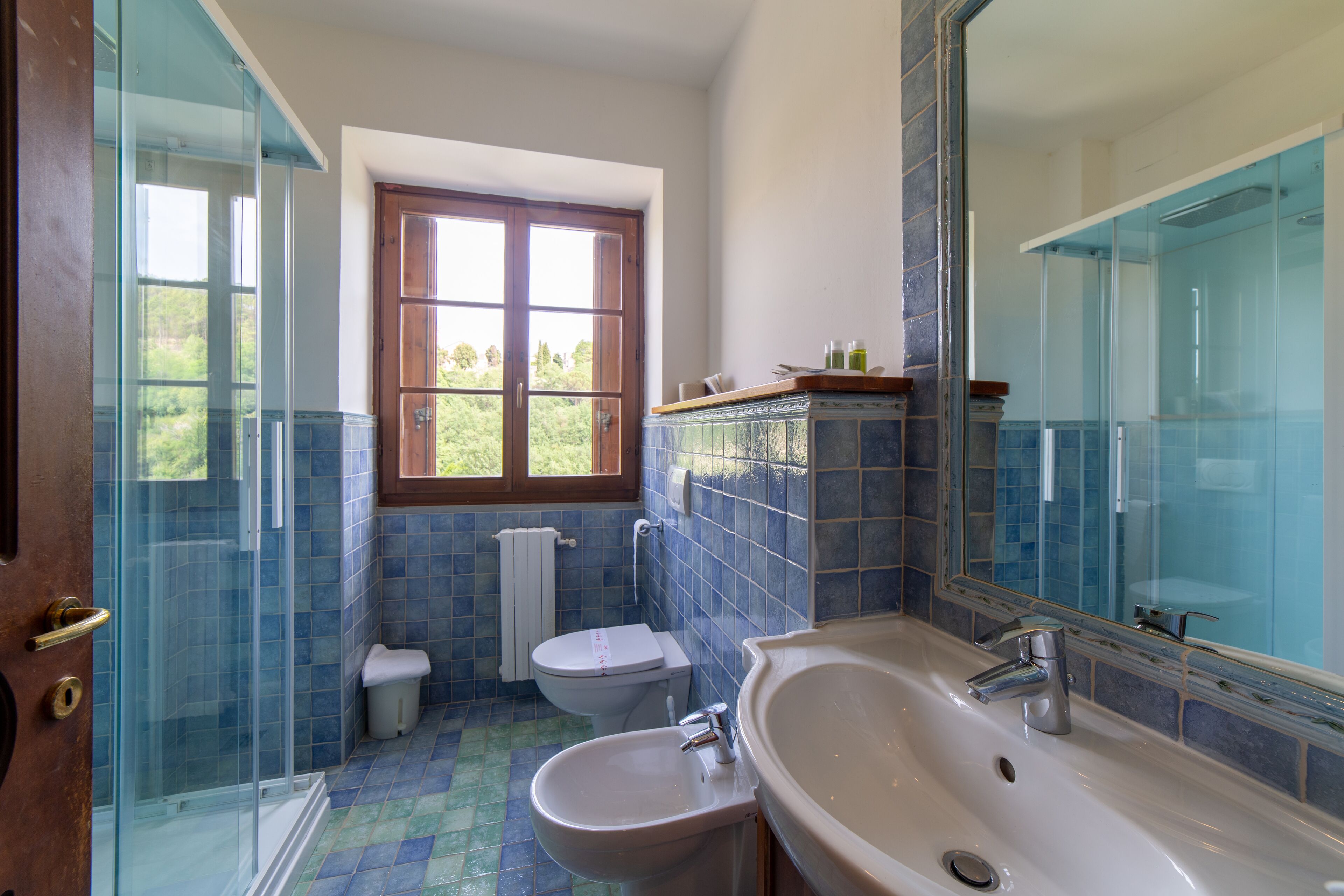 A bathroom with a glass shower enclosure, a toilet, a sink, and a window.