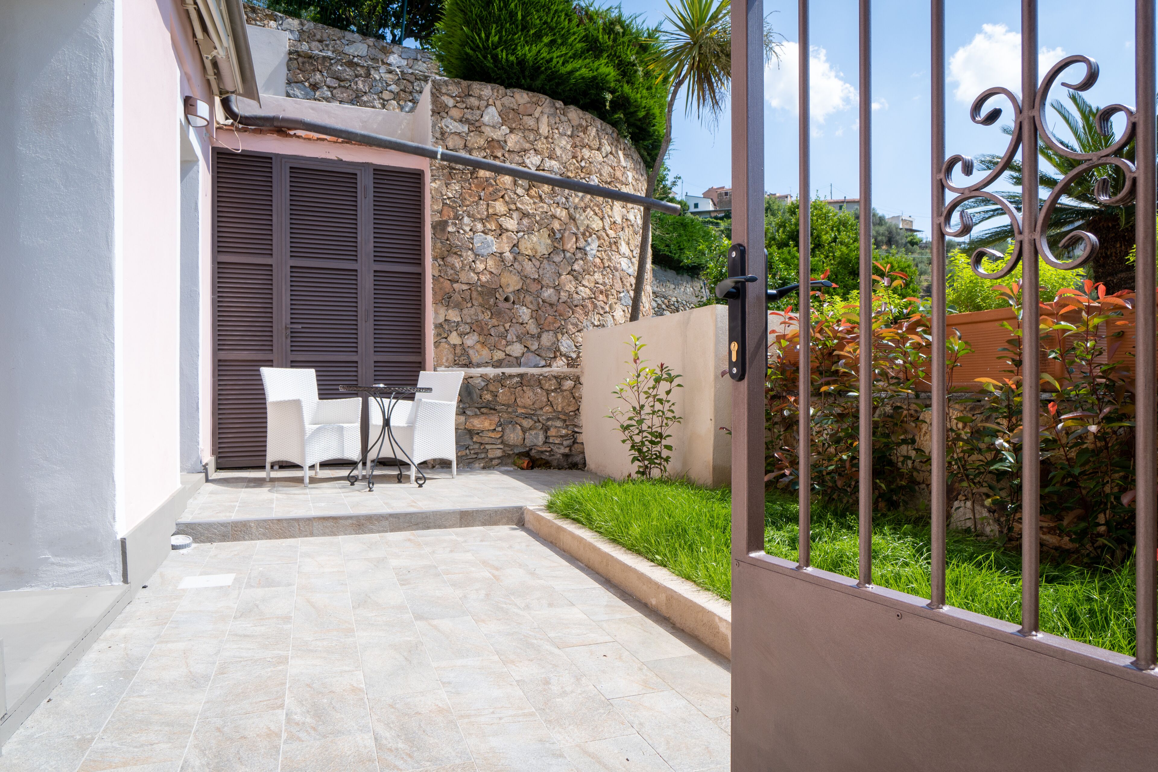Un patio con pared de piedra, una mesa con sillas y una reja de metal.