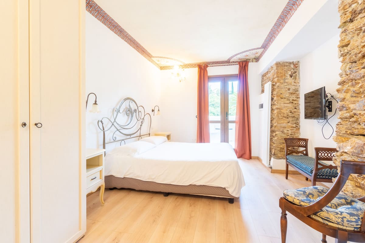 A bedroom with a bed, a nightstand, a chair, a TV, and a stone wall.