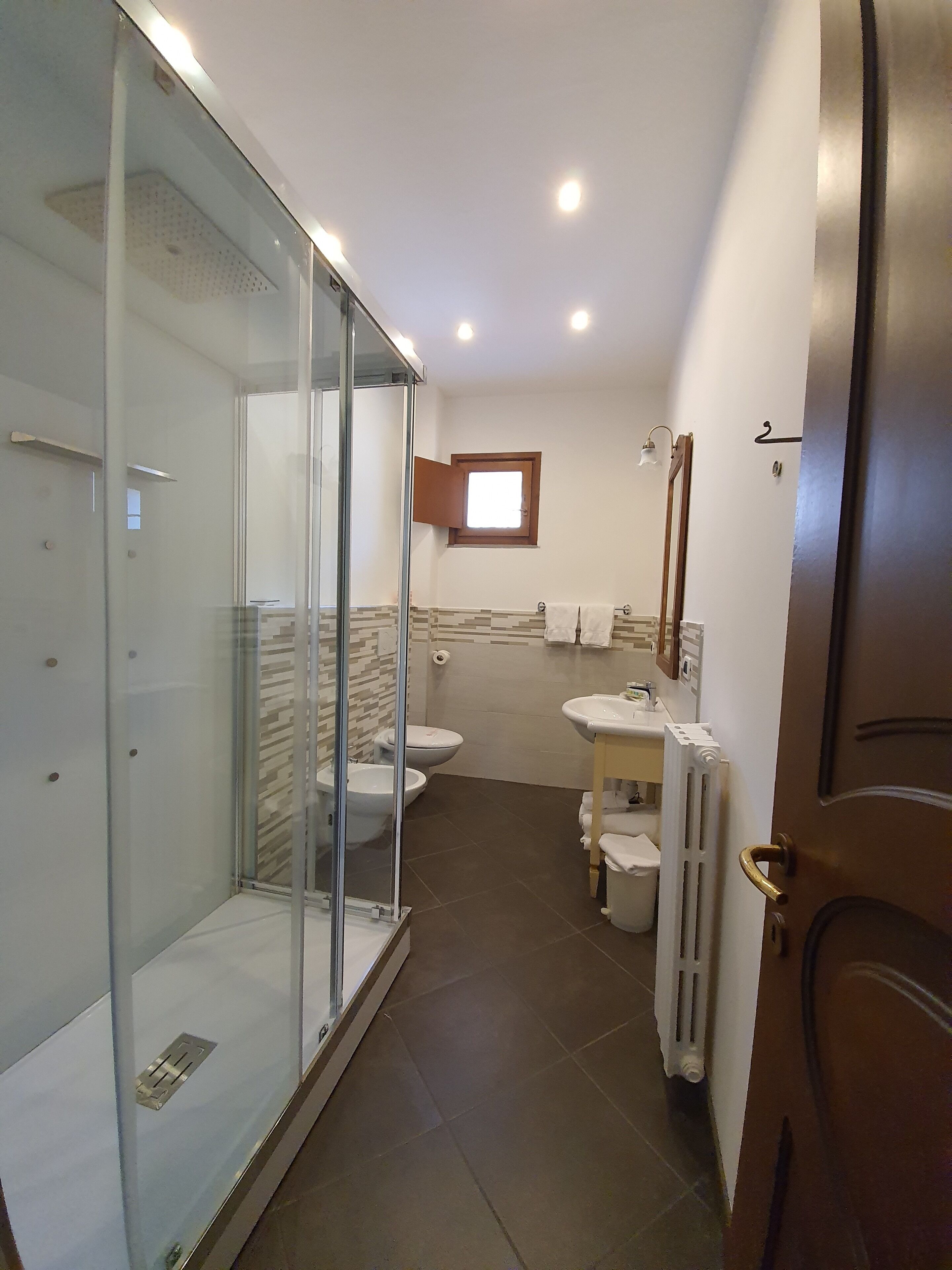 Un bagno moderno con box doccia in vetro, un water, un bidet, un lavandino e uno specchio.