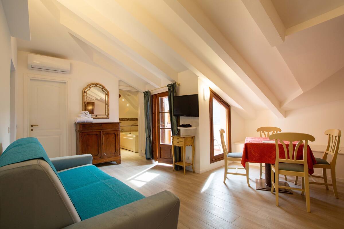 A cozy living room with a sofa, a dining table with chairs, a wooden cabinet, and a television.