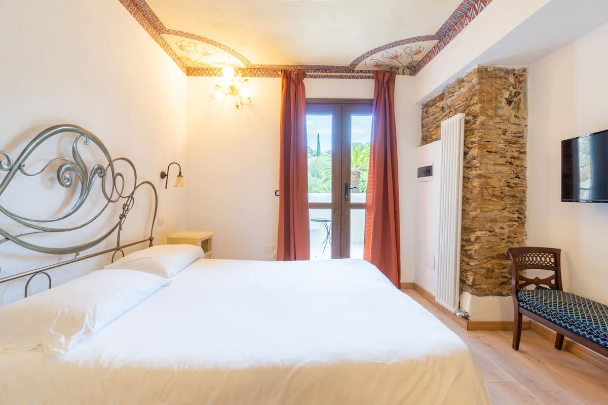 A bedroom with a bed, a nightstand, a chair, a stone wall, a radiator, and a TV mounted on the wall.