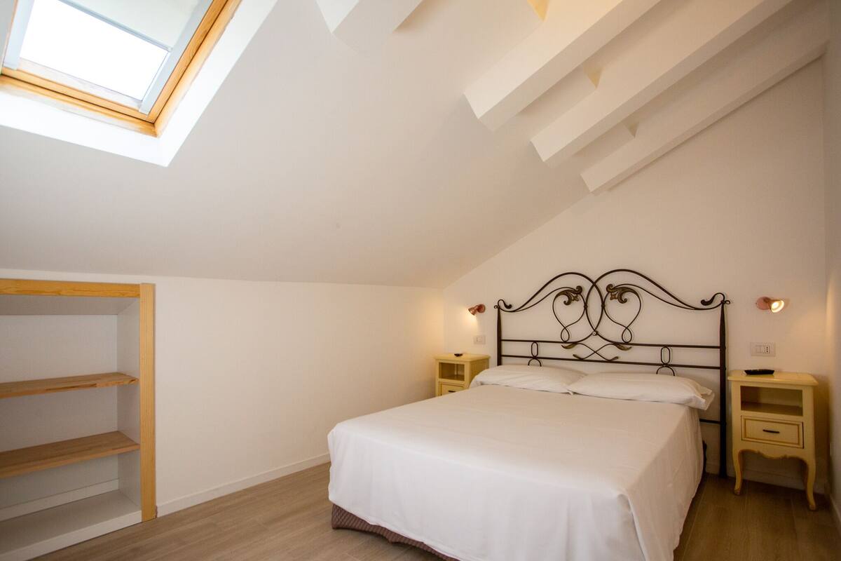 A bedroom with a skylight, a bed with white bedding, two bedside tables, and a wooden shelf unit.
