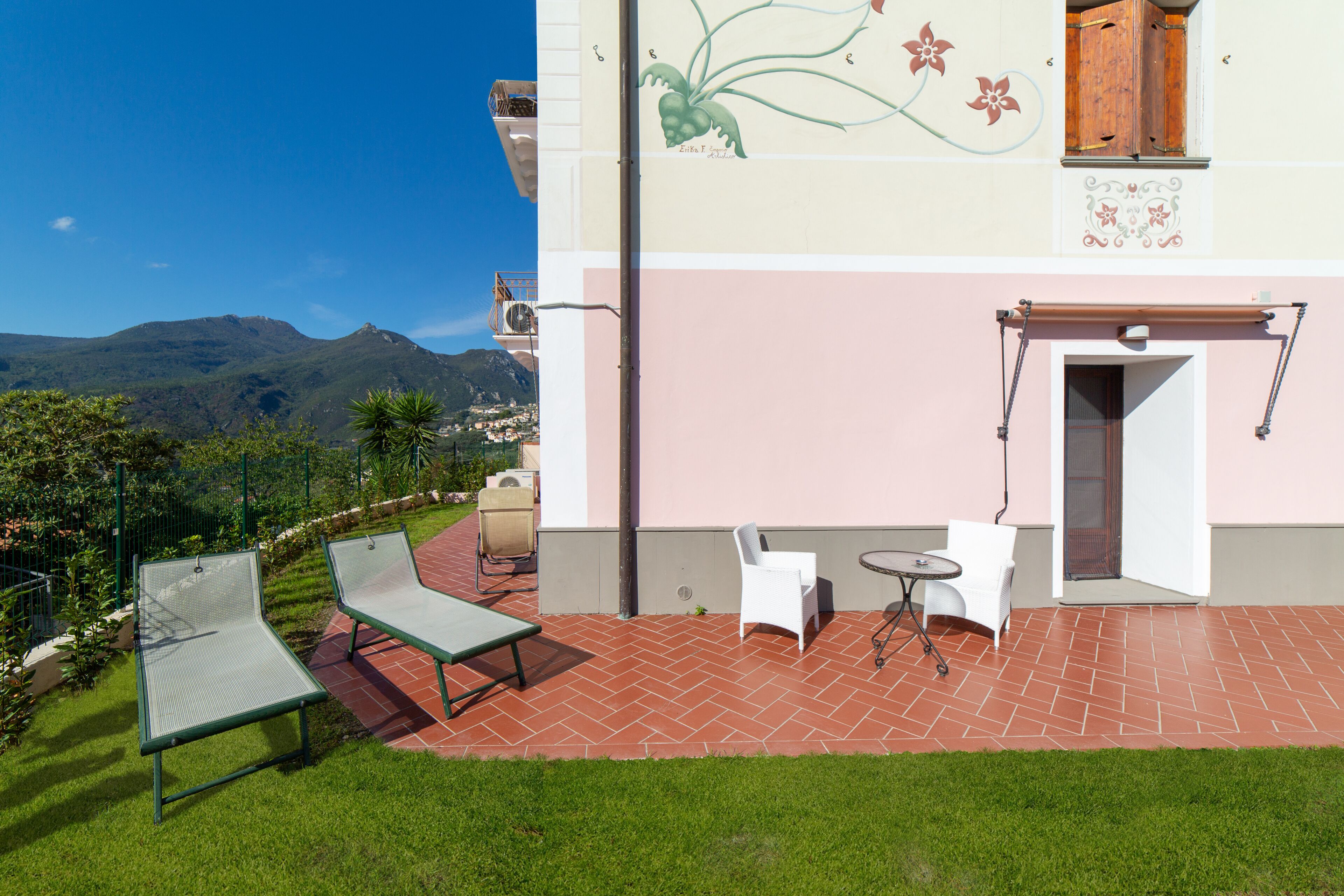 Un patio con un tavolo in metallo verde, due sedie bianche e un tavolino rotondo.