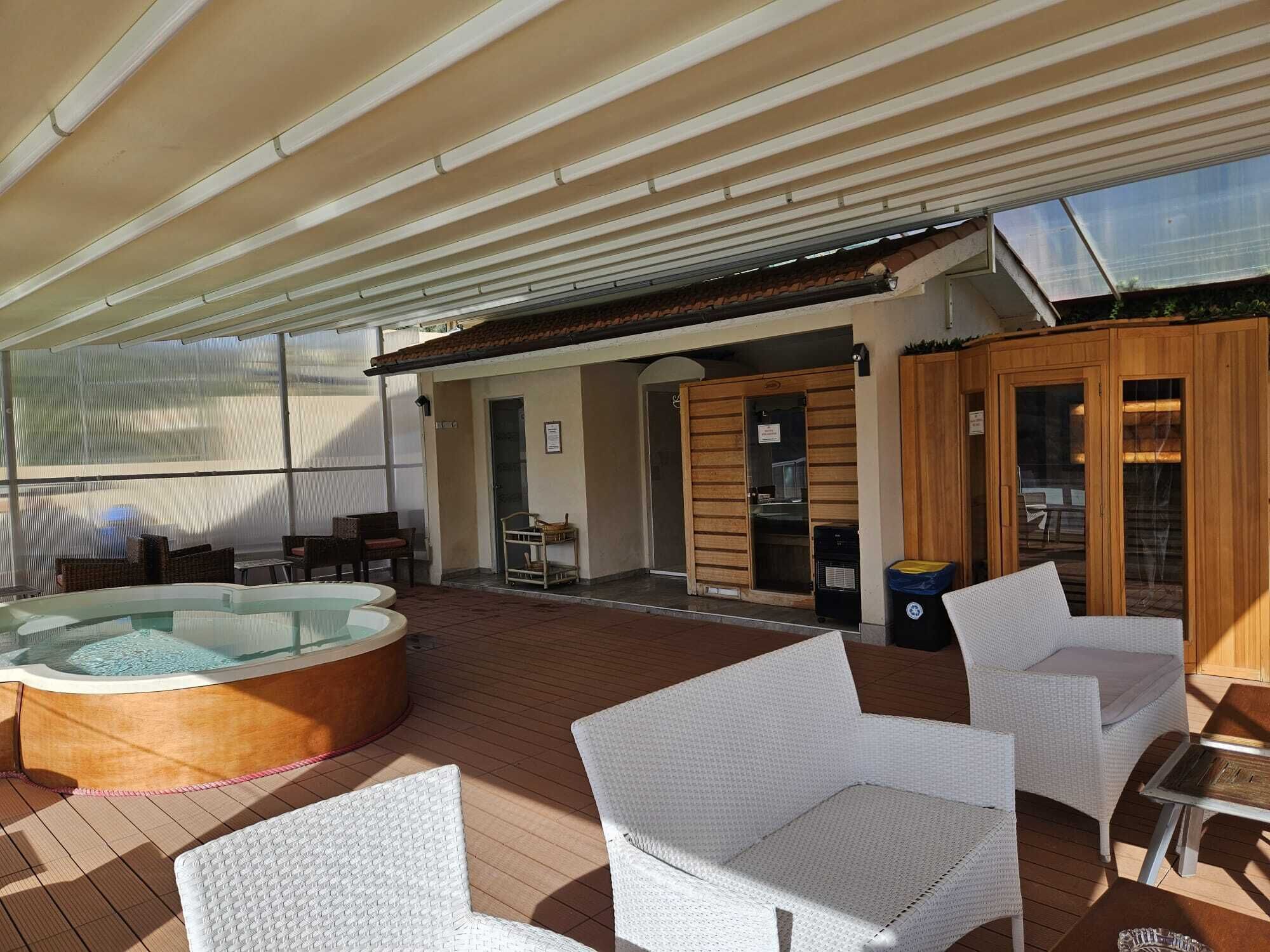 A covered outdoor area with a hot tub, wicker chairs, and a sauna.