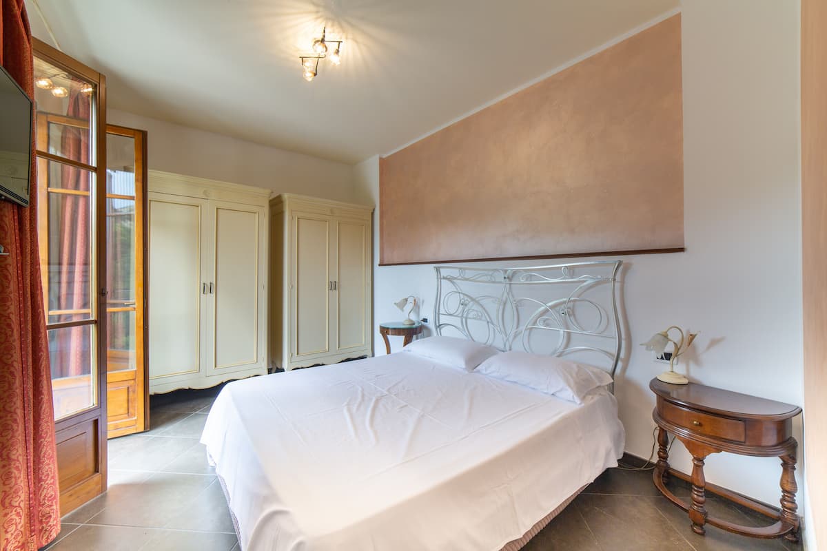 A bedroom with a large bed, a nightstand, a mirror, and a wardrobe.