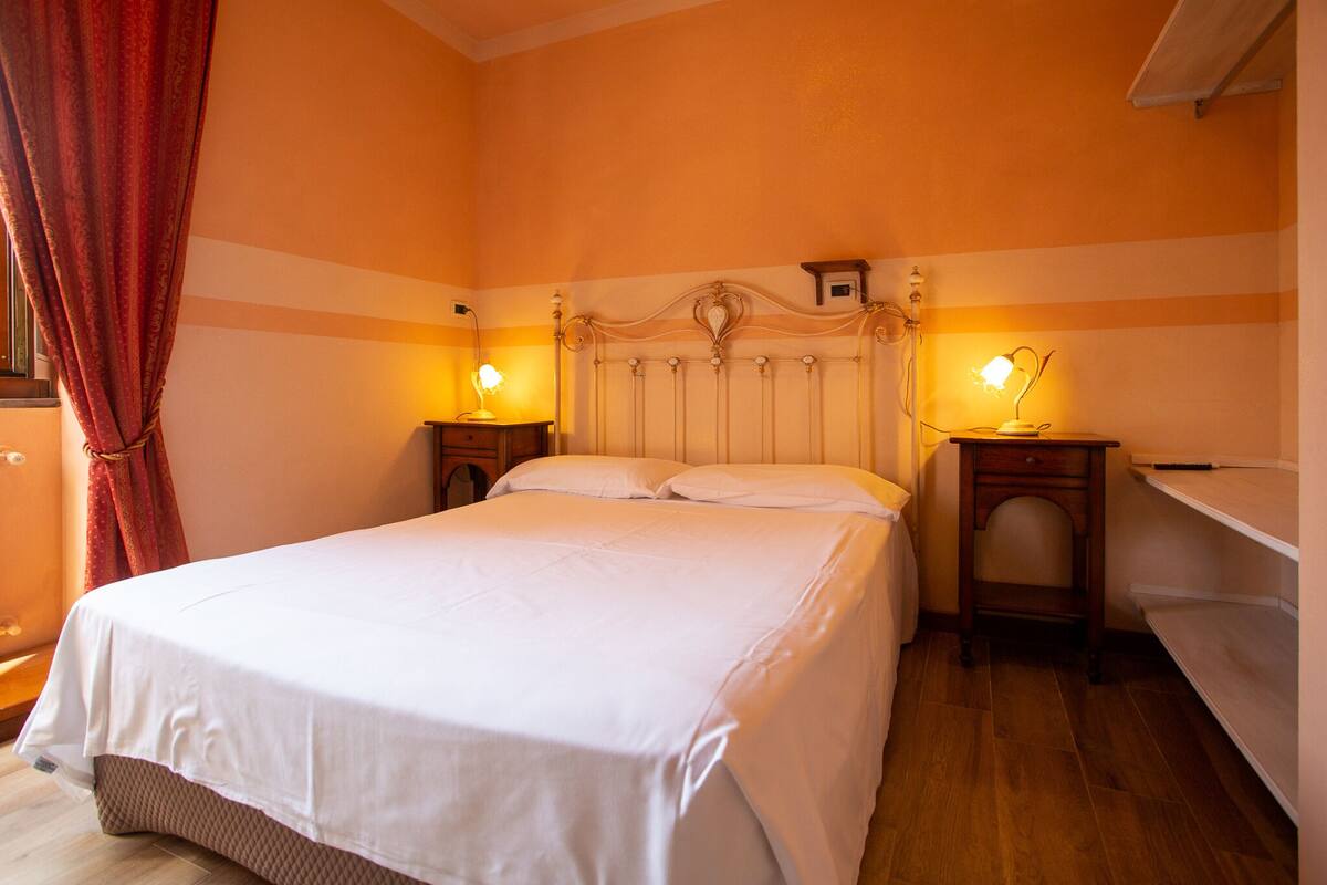 A neatly made bed in a room with striped walls, two bedside tables with lamps, and a wooden floor.