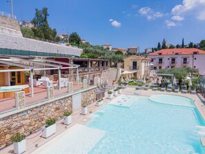 A pool area with lounge chairs and umbrellas, a stone wall, and a building with a red roof in the background. - Relais Il Casale (Tovo San Giacomo)