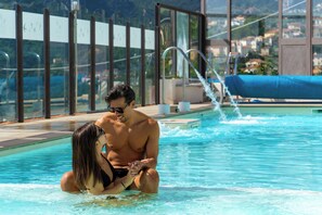 Una piscina con agua azul cristalina, una silla de descanso y una vista de una zona residencial al fondo.