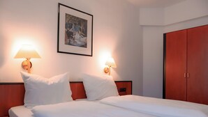 A hotel room with a bed, two bedside lamps, a framed picture on the wall, and a wardrobe. - Hotel Brößler (Stockstadt am Main)