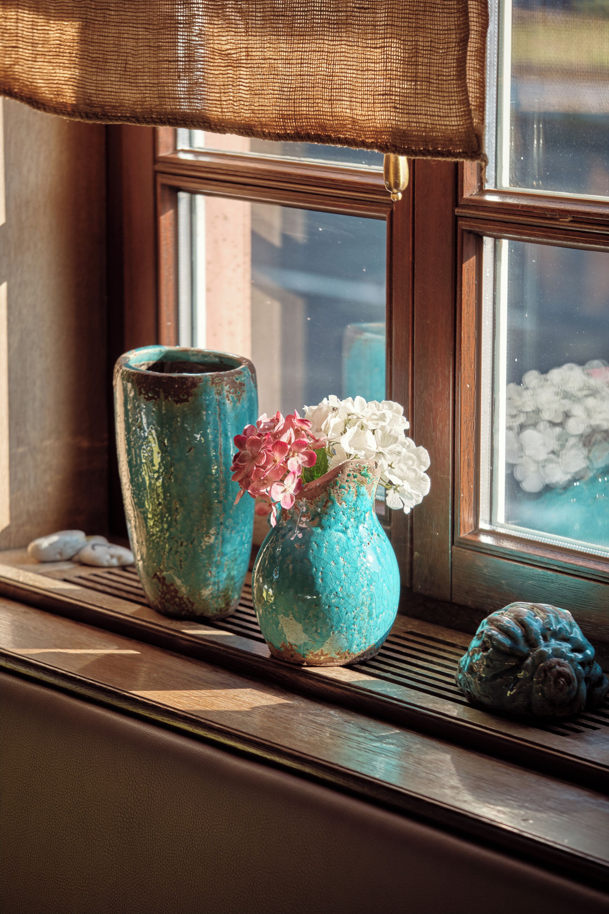 A window sill with two ceramic vases, one with flowers and the other empty, and a decorative object beside them.