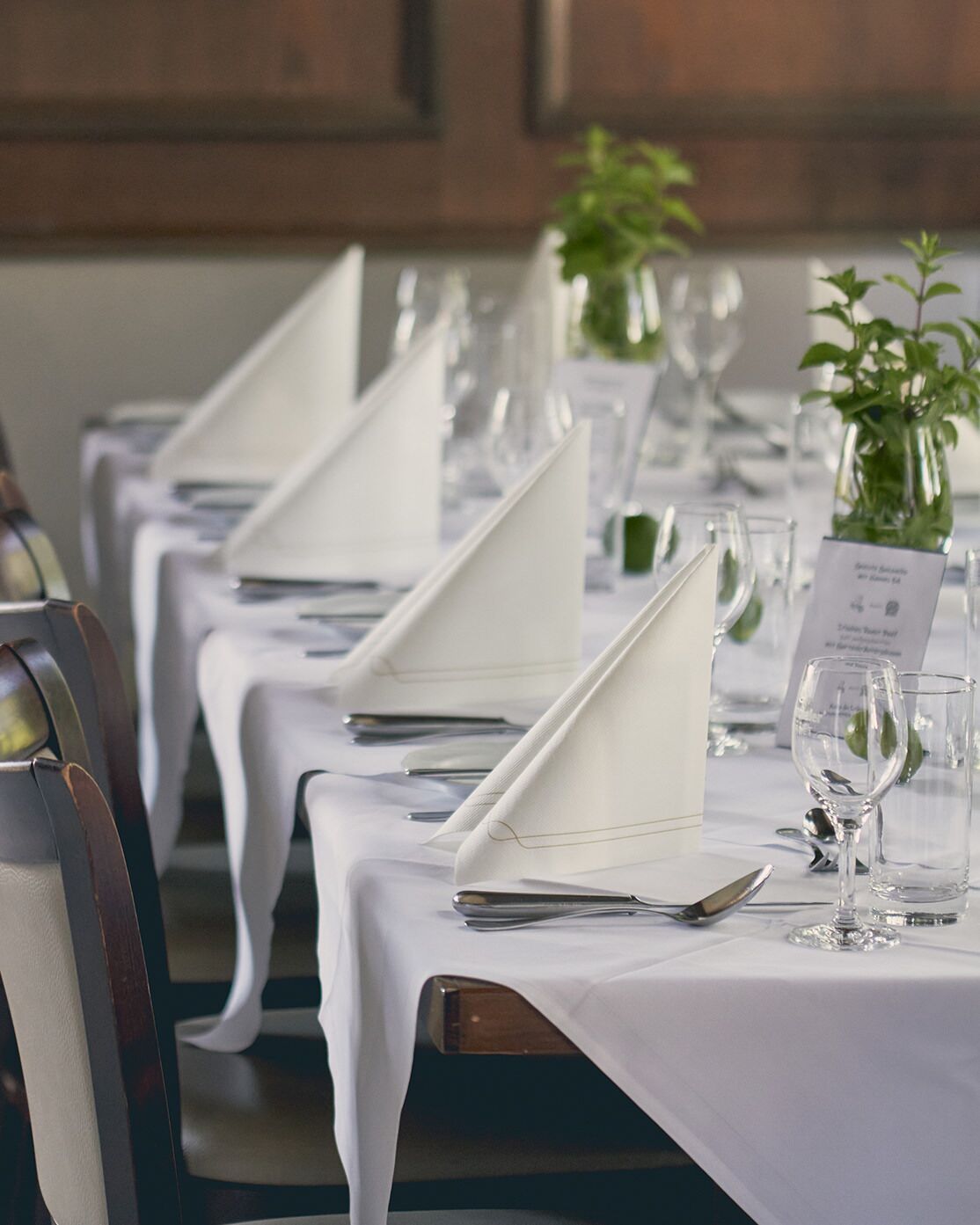A dining table set with white tablecloths, silverware, and wine glasses, with a menu card visible.