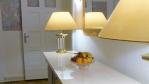 Um corredor com uma porta branca, um espelho, uma luminária e uma fruteira sobre um balcão branco.