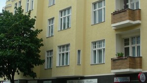 Um edifício com vários andares, fachada amarela, várias janelas e varandas com plantas.