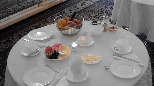 Uma mesa de jantar redonda posta com pratos brancos, talheres e uma cesta de frutas.