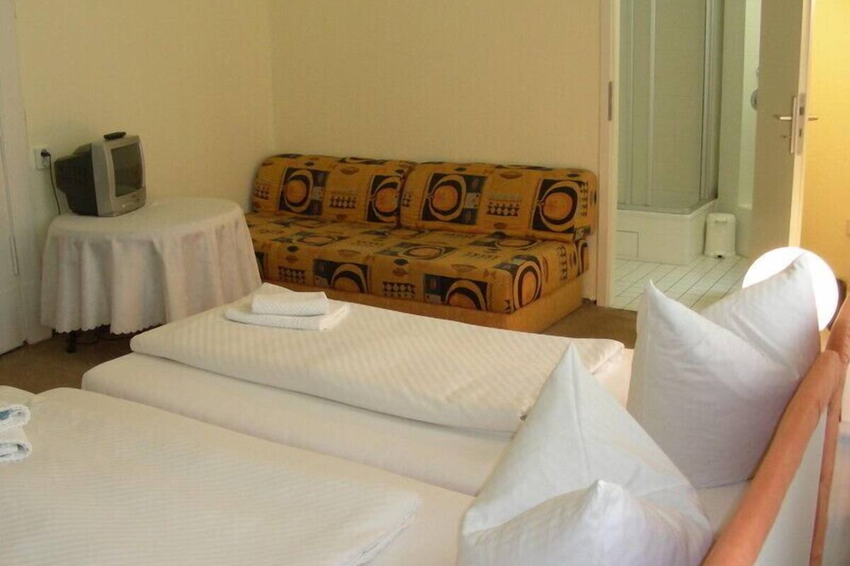 Une chambre d’hôtel avec deux lits, un canapé, une petite table avec un téléviseur et un espace douche.