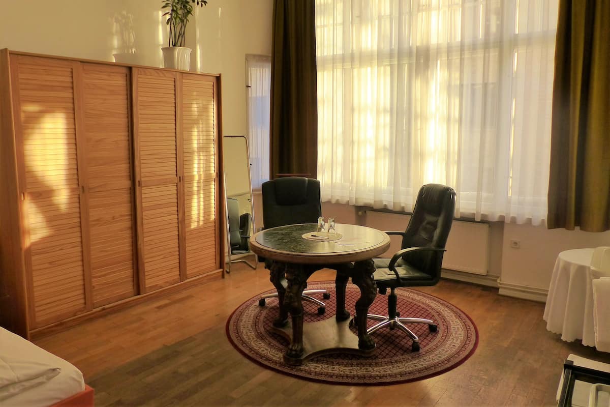 Une pièce comprenant une table ronde, deux chaises, une armoire et une fenêtre ornée de rideaux légers.