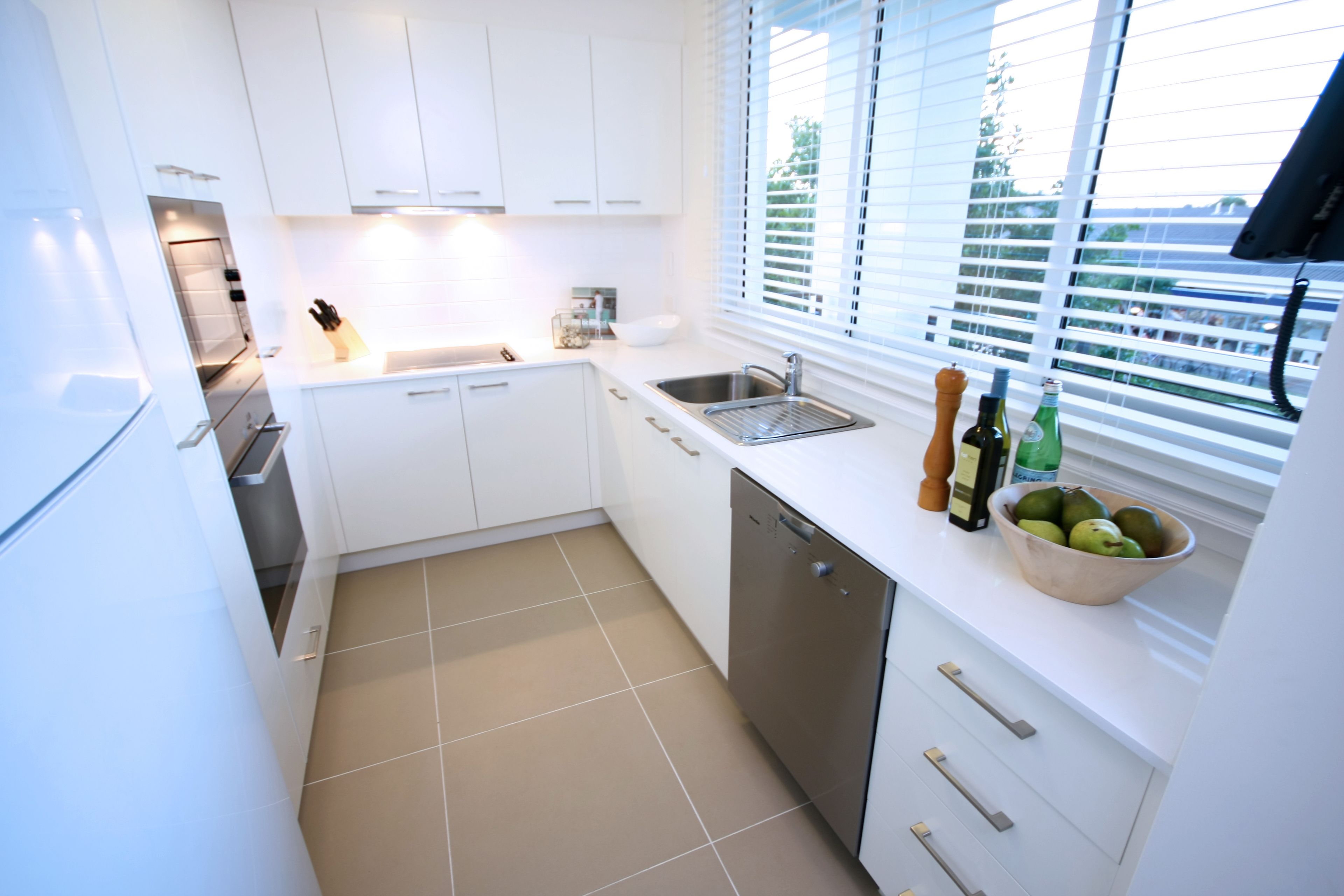 A modern kitchen with white cabinets, a dishwasher, a sink, and a window with blinds.