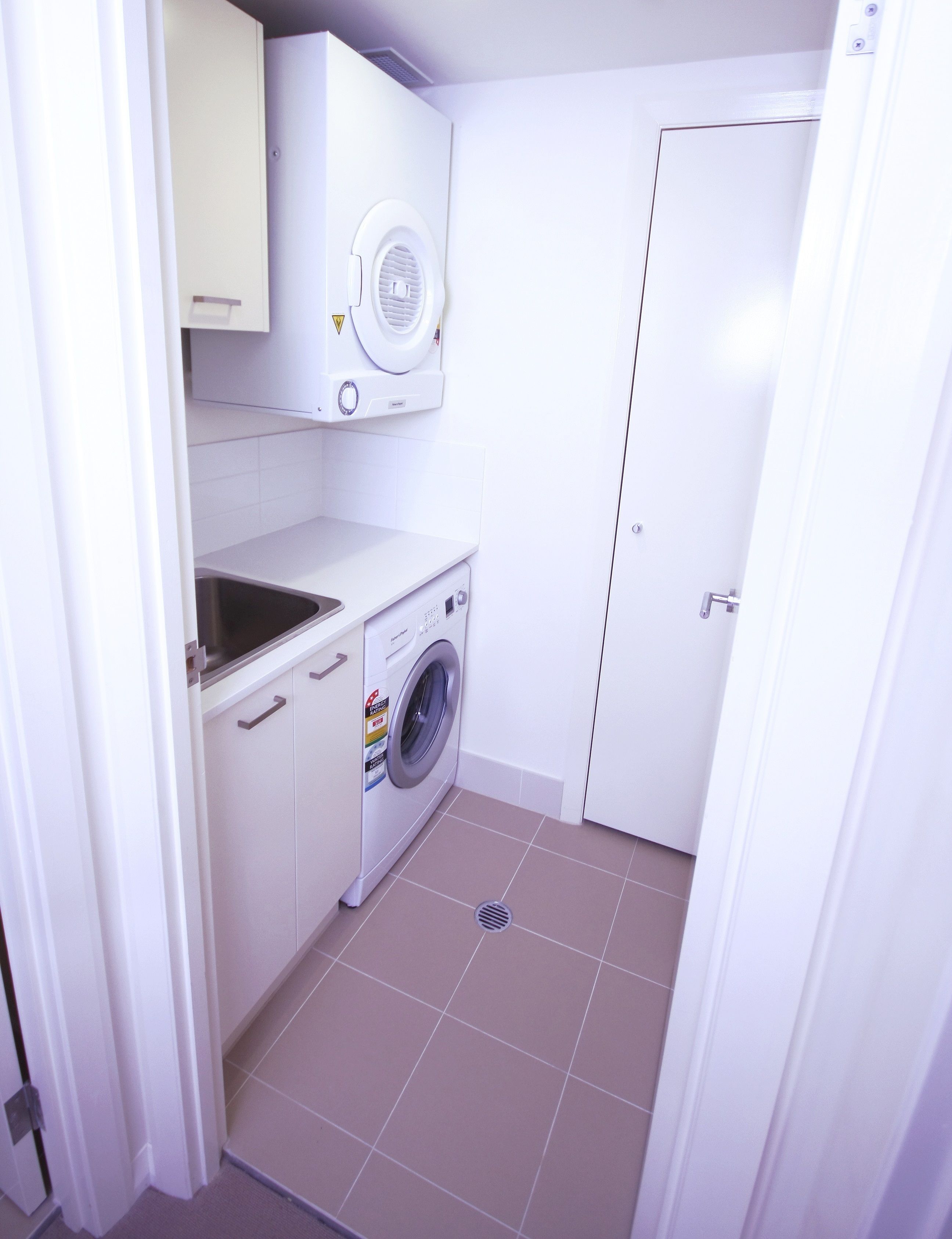 Une petite buanderie comprenant un lave-linge, un évier et une porte.