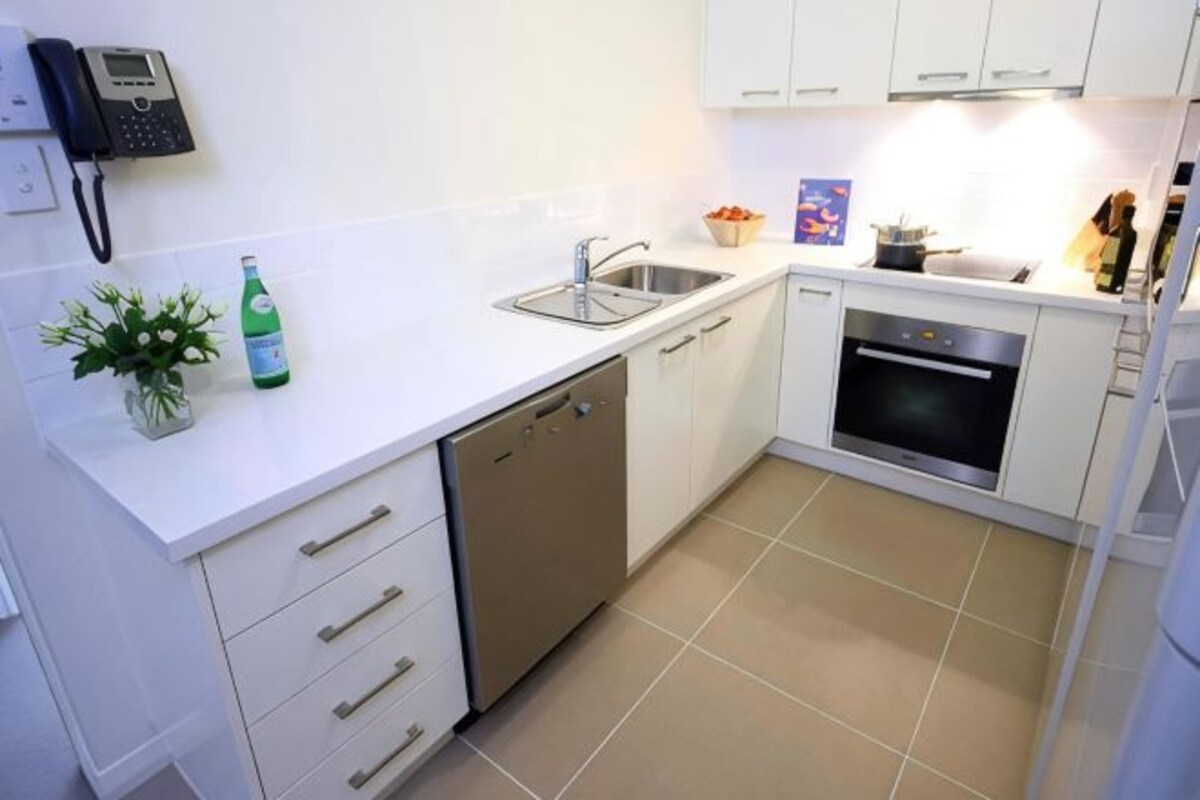 A compact kitchen with a dishwasher, oven, and a phone on the wall.