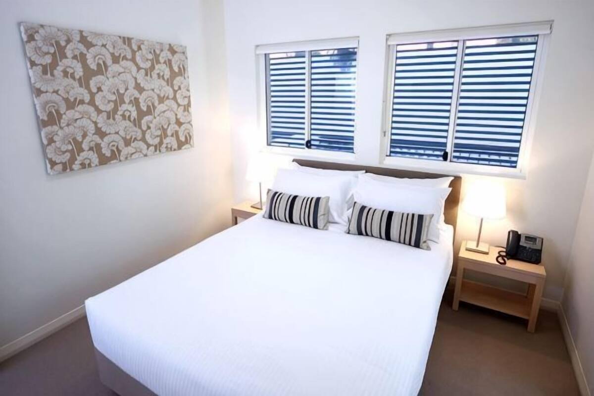 A neatly made bed with white bedding, two bedside tables with lamps, and a wall-mounted artwork.