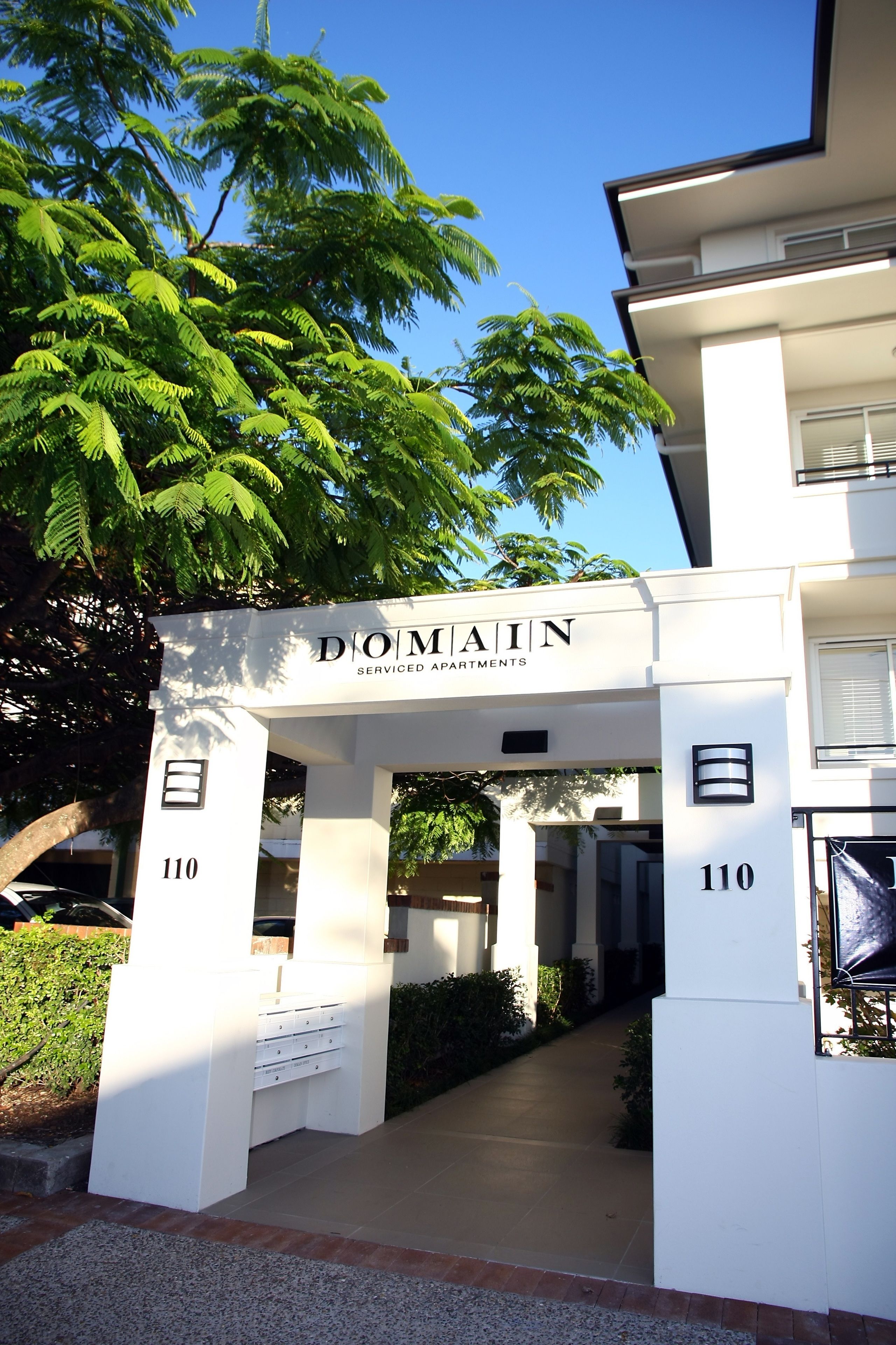 A white building with a sign reading "DOMAINE Serviced Apartments" and the number 110.
