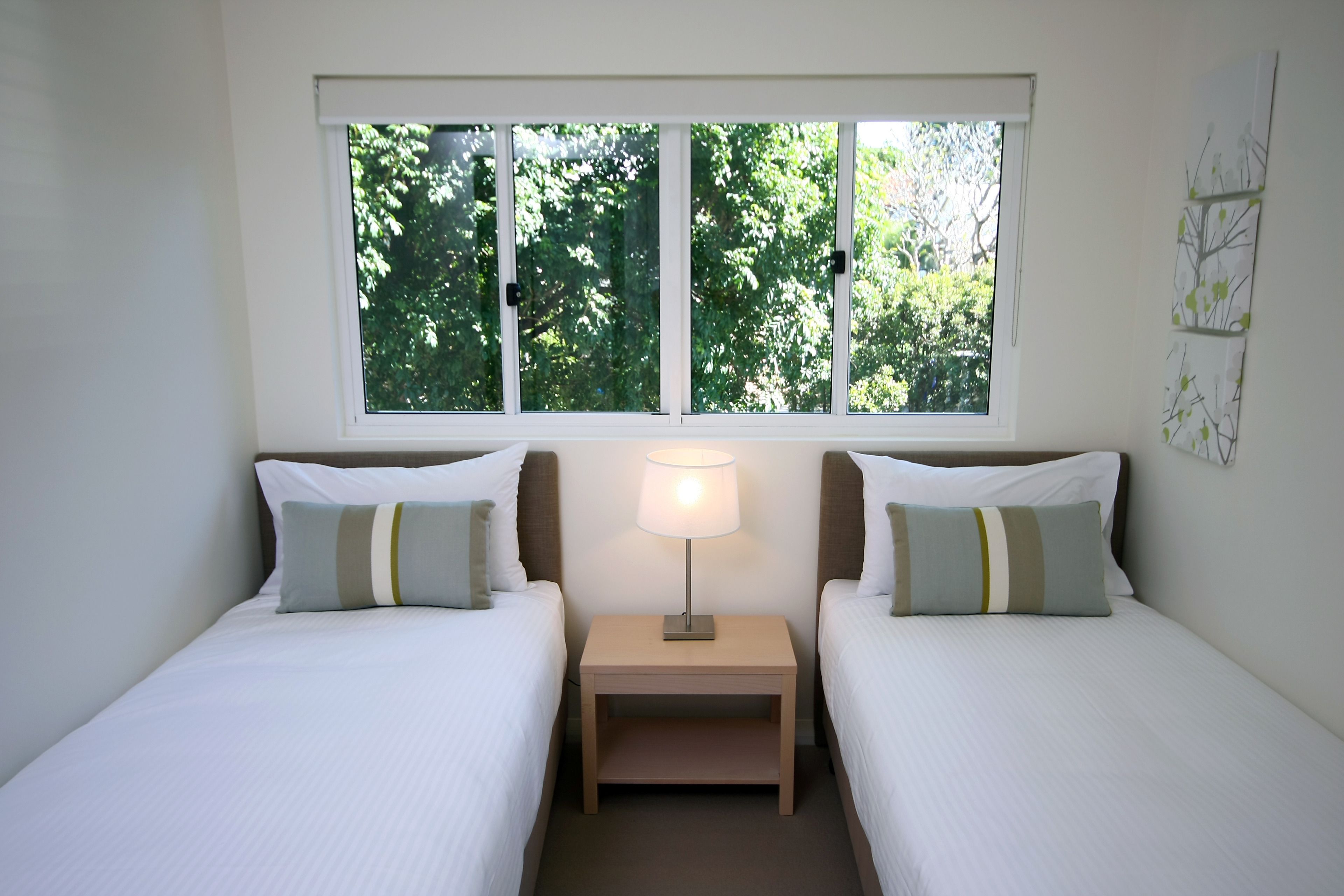 Une chambre avec deux lits, une table de chevet avec une lampe et une fenêtre donnant sur des arbres.