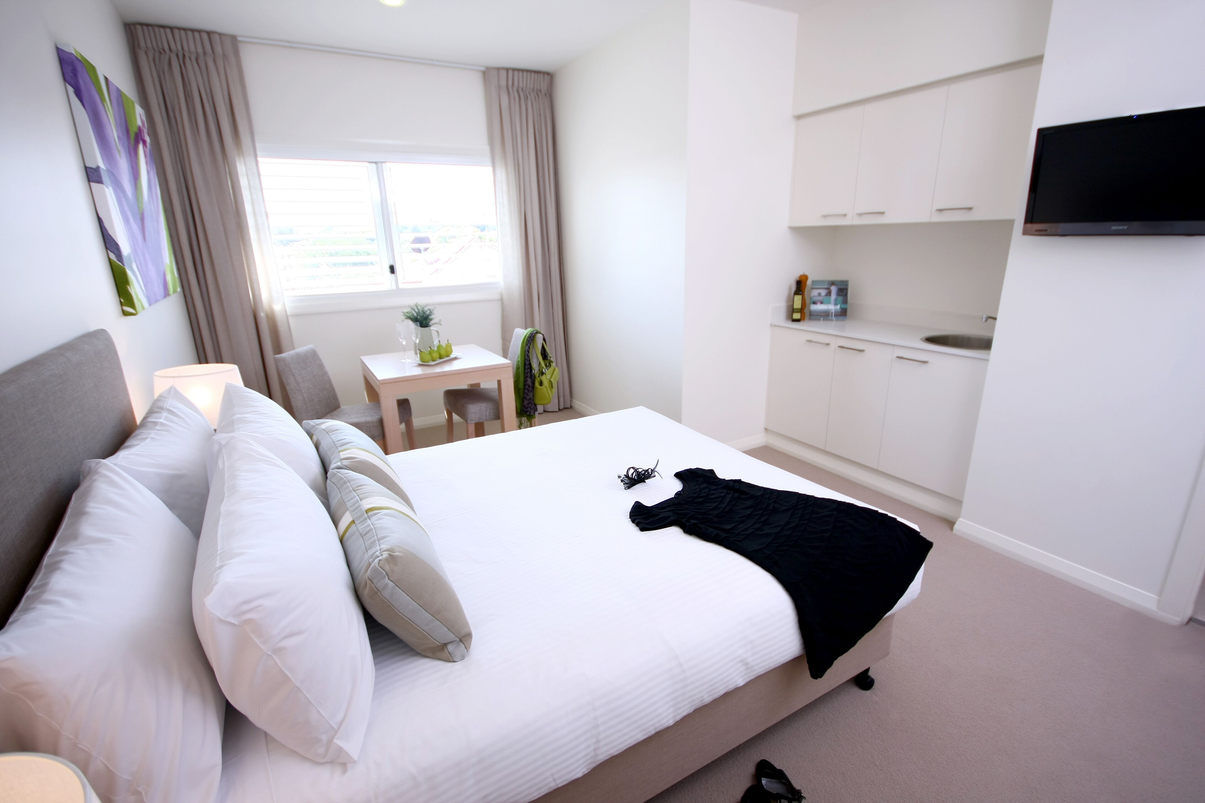 Een hotelkamer met een groot bed, een bureau, een stoel, een aan de muur bevestigde televisie en een kitchenette.