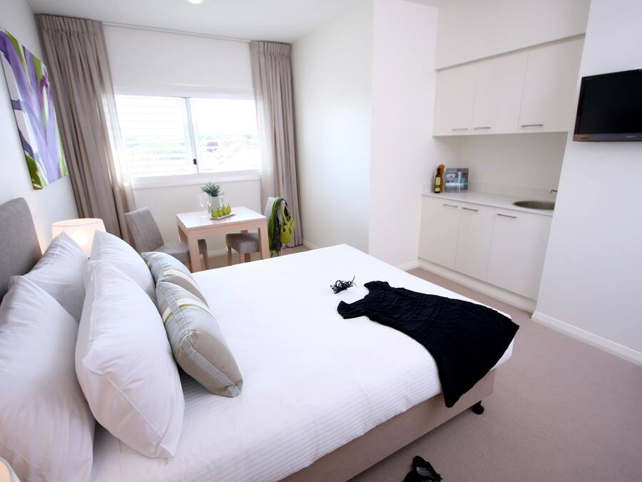 Een hotelkamer met een groot bed, een bureau, een stoel, een aan de muur bevestigde televisie en een kitchenette.