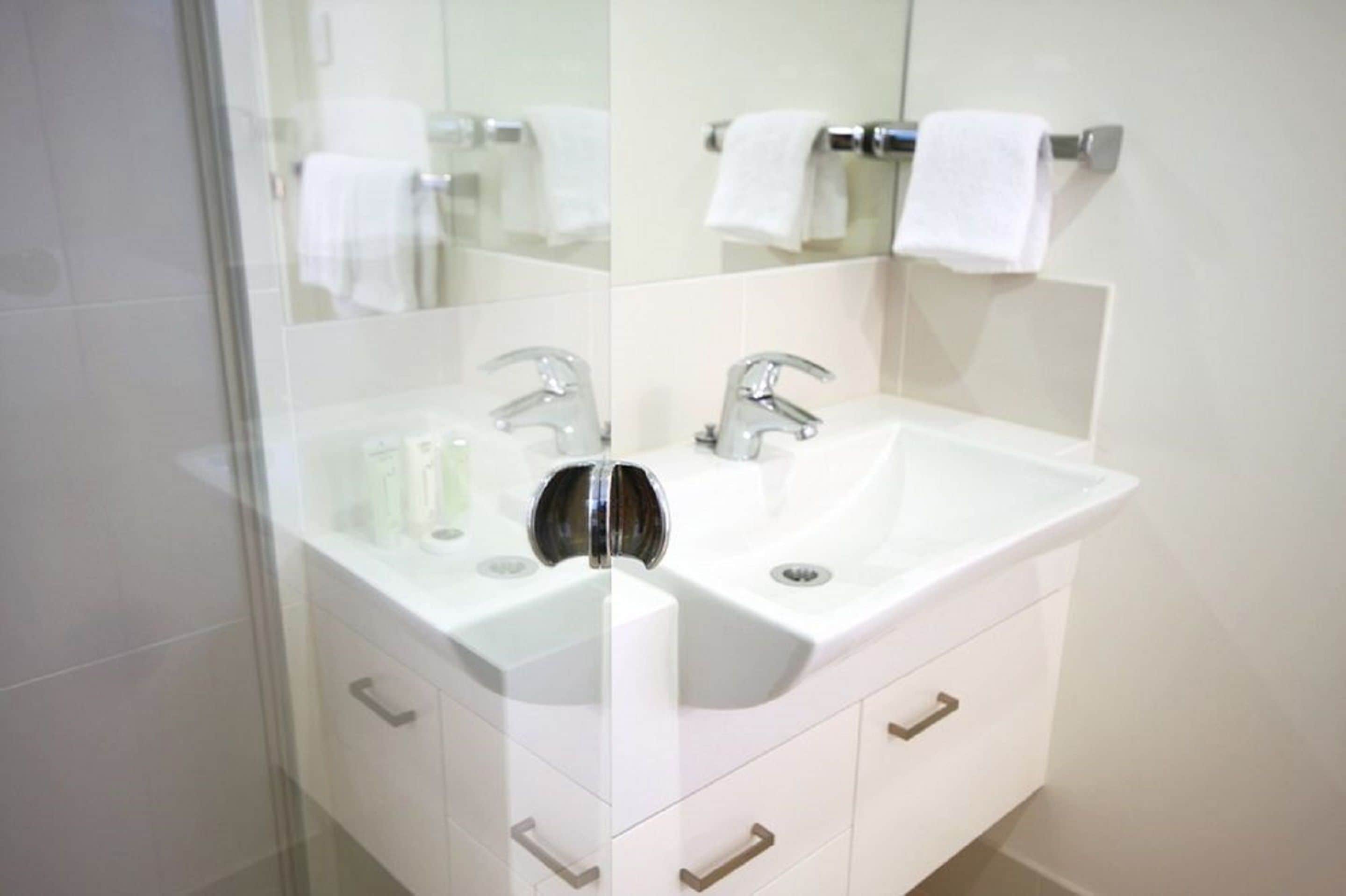 Een moderne badkamer met een wit wastafel, twee kranen en een douchecabine van glas.