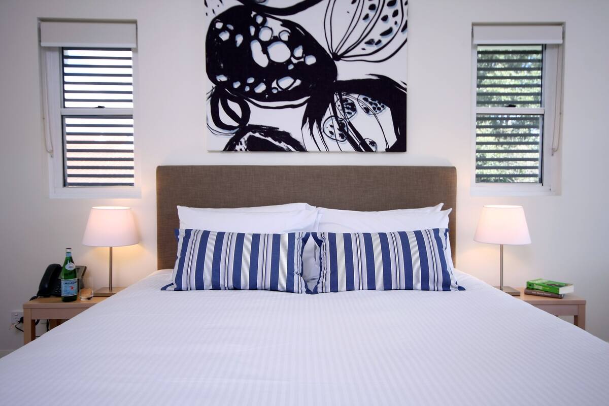 A neatly made bed with striped pillows, a wall art piece above it, and two bedside lamps on either side.