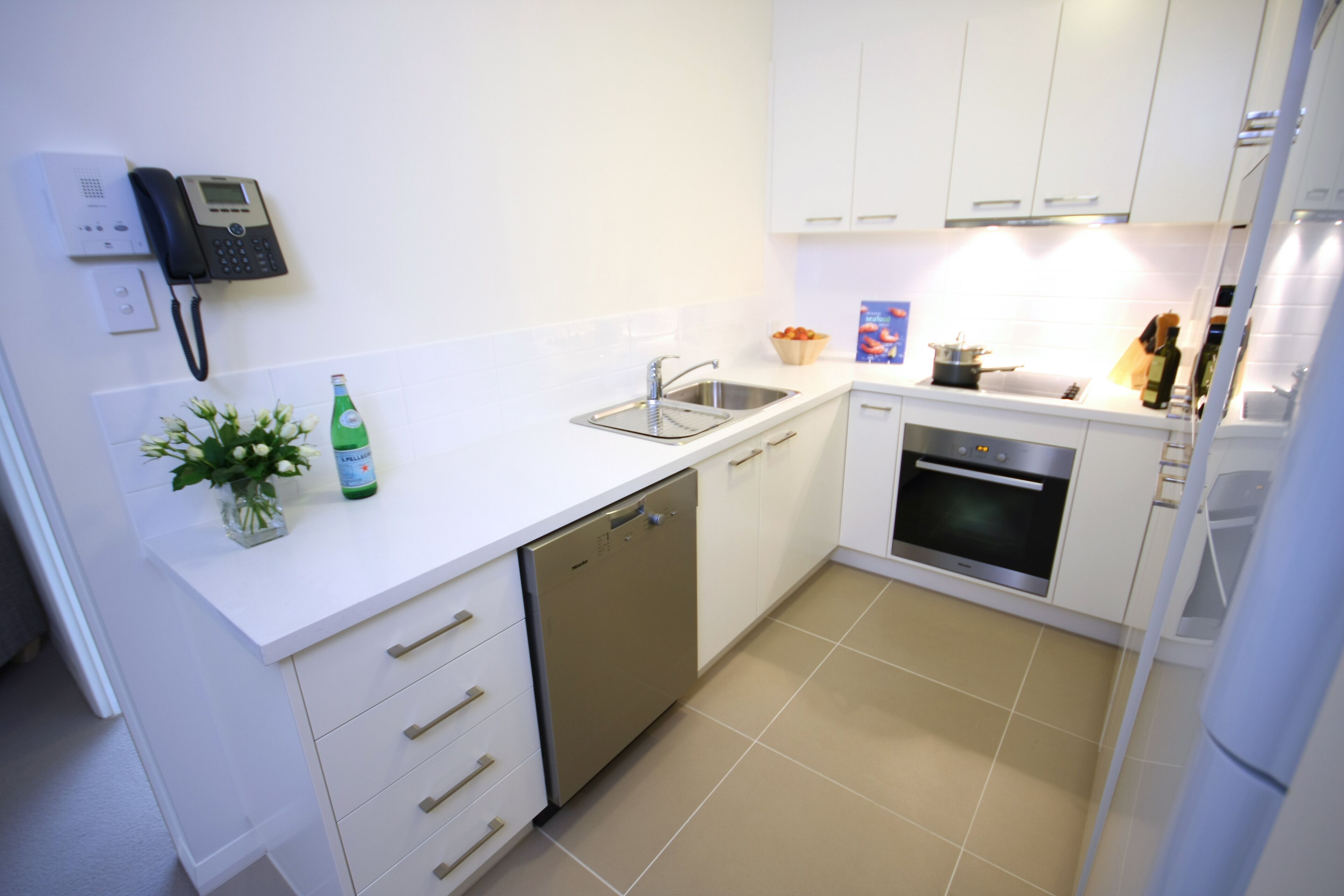 A modern kitchen with white cabinets, a dishwasher, an oven, and a sink.