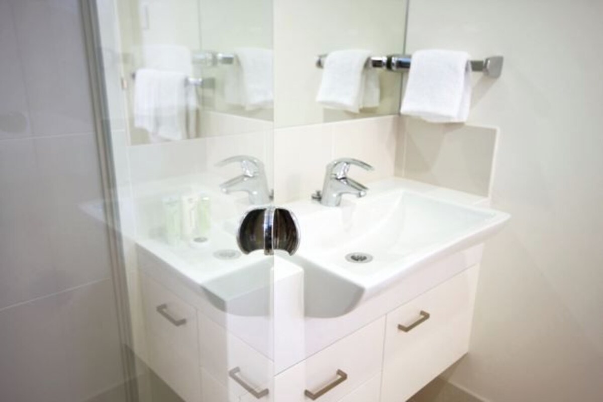 A bathroom with a white sink, two faucets, and a mirror. There are two towels hanging on the wall.