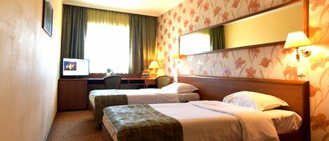 A hotel room with two single beds, a desk with a chair, a television, and a large mirror.