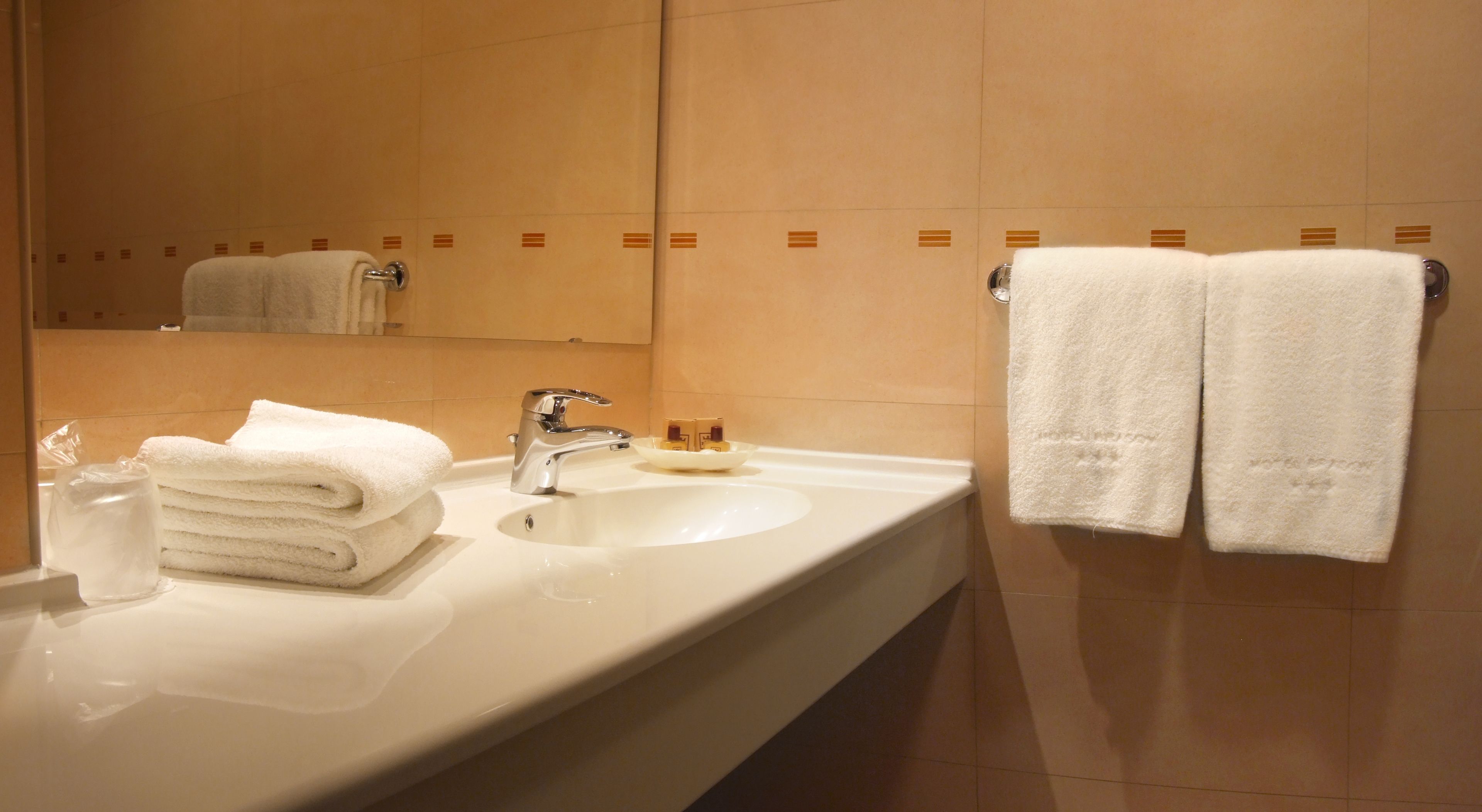 Un bagno d'albergo con un lavandino bianco, uno specchio e due asciugamani bianchi appesi a un portascopevoli.